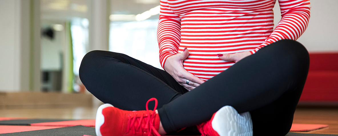 Pregnant woman in a striped shirt sitting cross-legged on a mat and cradling her abdomen.