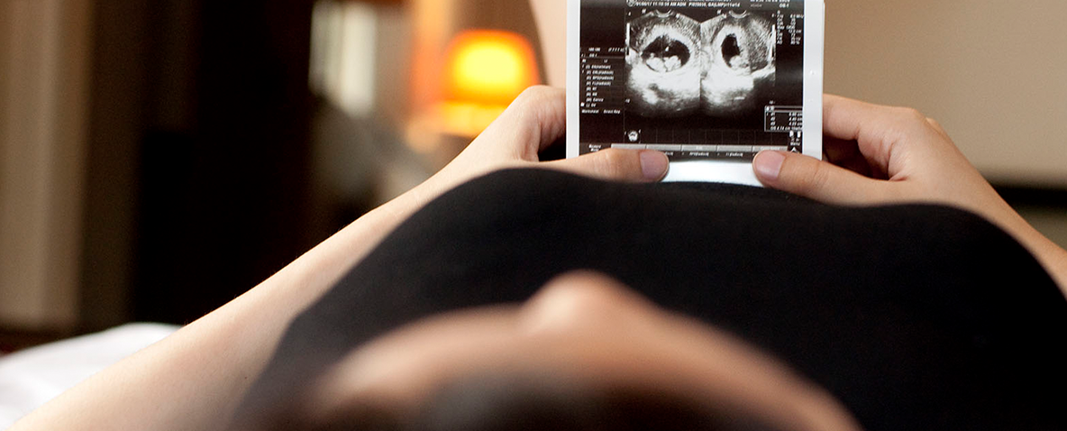 Pregnant woman lying on her back in a hospital bed looking at a sonograph image.