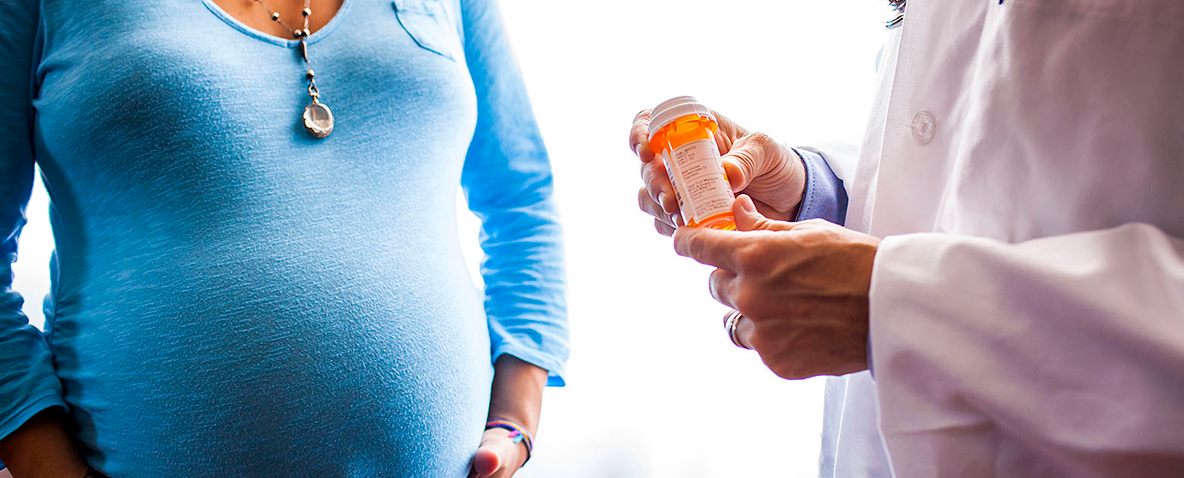 A doctor holding a prescription bottle while talking with a pregnant woman 
