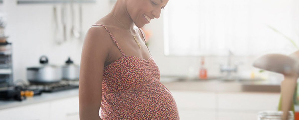 Pregnant woman smiling and looking down in a sunlit kitchen